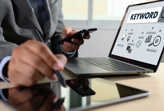 Person using a smartphone and laptop showing SEO keyword analysis, representing an SEO-optimized website structure